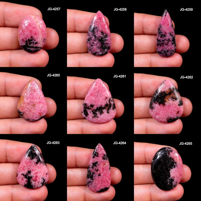 May include: Nine polished rhodochrosite gemstones in various shapes, including oval and teardrop. The stones feature a vibrant pink hue with black and gray veining. Each stone is held in a hand against a black background.