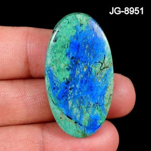 May include: An oval-shaped polished gemstone featuring a vibrant mix of bright blue and mottled green patterns with dark veining throughout. The stone displays a smooth, glossy surface texture and is labeled with the text JG-8951 in the corner.