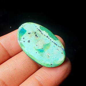 May include: Oval shaped turquoise cabochon gemstone with green, blue, and white patterns and black inclusions.