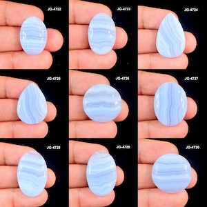 Pode incluir: Uma coleção de nove pedras preciosas de ágata rendada azul polidas em várias formas, incluindo oval, gota e redonda. Cada pedra exibe um padrão listrado de tons azuis claros e escuros. As pedras preciosas são exibidas em um fundo preto.