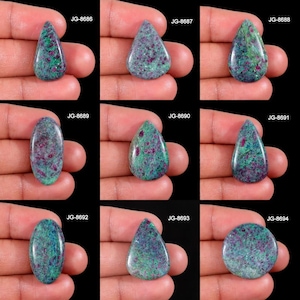 May include: Nine polished gemstones with a mix of shapes, including teardrop, oval, and round. The stones feature a mottled pattern of green, red, and blue-gray hues. Each stone is labeled with a unique code: JG-8686 through JG-8694.