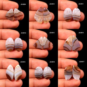 May include: A collection of polished agate gemstone pairs in various shapes, including teardrop, oval, and triangular. The stones feature bands of white, brown, and tan hues, with a glossy finish. Each pair is displayed against a dark background.