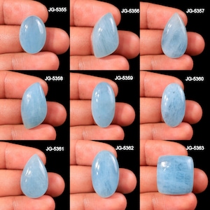May include: Nine aquamarine gemstones in various shapes, including oval, teardrop, and square, are displayed against a black background. Each stone has a pale blue color and is held in a hand. The image includes the text "JG-5355" through "JG-5363".