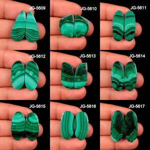 May include: A collection of nine pairs of polished malachite gemstones, each displaying unique patterns of green and black bands. The gemstones vary in shape, including teardrop, oval, and irregular forms. Each pair is labeled with a unique code.