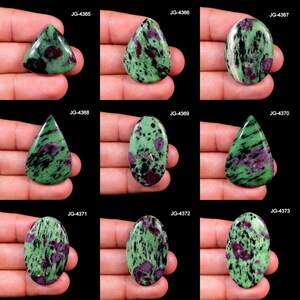 Może przedstawiać: Dziewięć polerowanych kamieni szlachetnych zoisytu w różnych kształtach, w tym owalnych, łezkowych i trójkątnych. Kamienie mają zieloną podstawę z czarnymi i czerwonymi wtrąceniami. Każdy kamień jest trzymany w dłoni na czarnym tle. Widoczne są kody produktów.