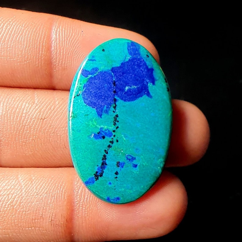 May include: Oval shaped cabochon gemstone with a blue and green pattern. The stone has a dark blue center with a green outer edge.
