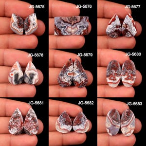 May include: A collection of nine pairs of polished agate gemstones, each with unique patterns of red, white, gray, and brown. The stones vary in shape, including teardrop, oval, and rectangular. Each pair is held in a hand against a black background.