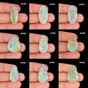 Könnte beinhalten: Eine Sammlung von neun Edelsteinen in verschiedenen Formen, darunter oval und tropfenförmig. Die Steine zeigen eine Mischung aus Farben, mit dominanten Grün- und Rosatönen sowie einigen Gelbtönen. Jeder Stein wird in einer Hand vor schwarzem Hintergrund gehalten.