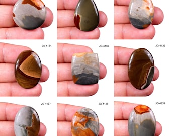 May include: Nine polished gemstone cabochons in various shapes, including round, teardrop, and oval. The stones display a range of colors, such as brown, gray, orange, and cream, with unique patterns and textures. Each stone is labeled with a "JG" code.