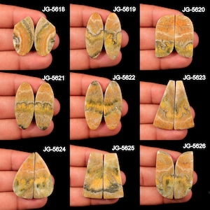 May include: A selection of gemstone pairs in diverse shapes, including oval, teardrop, and irregular forms. The stones display a blend of yellow, orange, and grey tones, with visible patterns and textures. Each pair is labelled with a unique code, such as JG-5618.