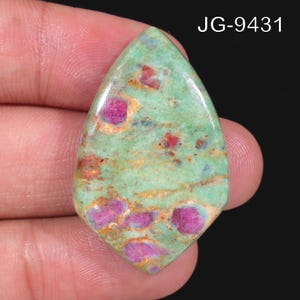 May include: A polished, pear-shaped gemstone featuring a light green base with embedded vibrant magenta and deep pink inclusions, accented by subtle tan and brown veining throughout the surface. The text JG-9431 is visible in the upper right corner.