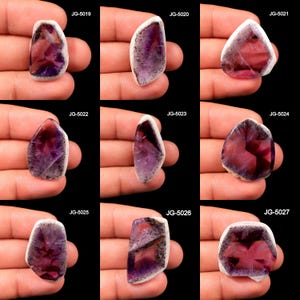 以下が含まれることがあります： 白縁と濃い紫色の中心を持つ、研磨されたアメジストの宝石が9つ表示されています。 各石はユニークな形状と内部パターンを持っています。 宝石にはJG-5019からJG-5027までのコードが付けられています。