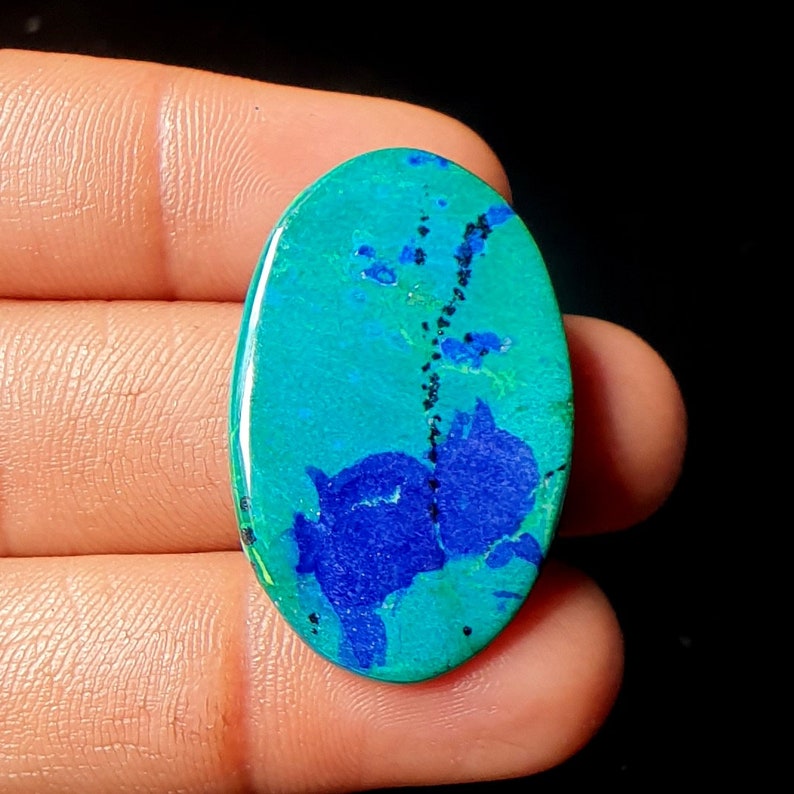 May include: Oval shaped cabochon gemstone with a blue and green pattern. The stone has a dark blue center with a green outer edge. The stone is set in a silver ring.