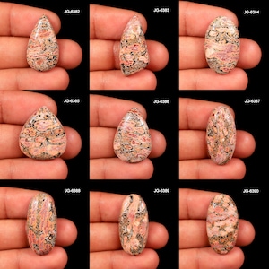 May include: Nine polished gemstones with a mix of shapes, including teardrop and oval. The stones have a mottled pattern of pink, black, and tan colors. Each stone is held in a hand against a black background. The labels JG-6382 through JG-6390 are visible.