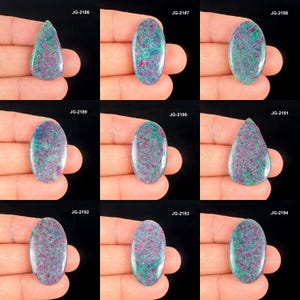 May include: Nine polished gemstones with a mix of colours, including red, green, and blue, are displayed. The gemstones vary in shape, with oval and teardrop forms. Each stone has a unique pattern and texture, set against a black background.