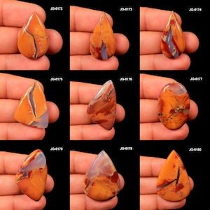 May include: A collection of nine polished gemstones in various shapes, including teardrop and oval. The stones feature a mix of orange, red, and gray hues with unique veining patterns. Each stone is held in a hand against a black background.