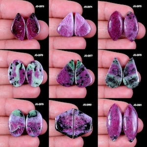 Könnte beinhalten: Eine Sammlung von neun Paaren polierter Edelsteine in verschiedenen Formen, darunter Tropfen, Oval und Dreieck. Die Steine weisen eine Mischung aus Farben auf, hauptsächlich tiefrot und grün, mit schwarzen Einschlüssen. Jedes Paar wird vor dunklem Hintergrund präsentiert.