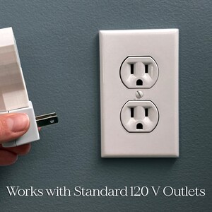Op de afbeelding: Een witte elektrische contactdoos met twee stopcontacten wordt getoond naast een wit insteekapparaat. Het insteekapparaat wordt in het stopcontact gestoken. De tekst "Works with Standard 120 V Outlets" staat onderaan.