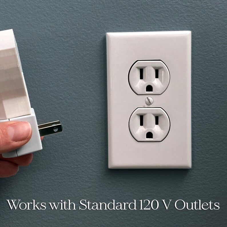 May include: A white electrical outlet with two receptacles is shown next to a white plug-in device. The plug-in device is being inserted into the outlet. The text "Works with Standard 120 V Outlets" is at the bottom.