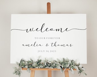 May include: White welcome sign with black calligraphy text that reads "Welcome to our forever Amelia & Thomas July 30, 2023".