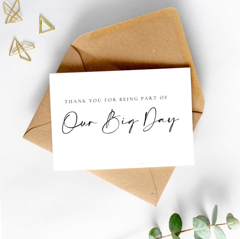 May include: White card with the text "Thank you for being part of Our Big Day" in black script font. The card is sitting on a brown envelope.