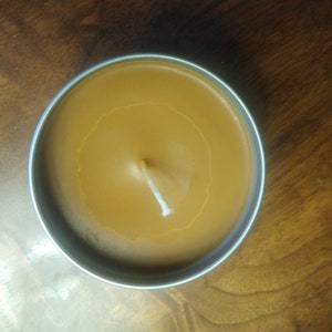 Könnte beinhalten: Eine braune Kerze in einer silbernen Dose mit einem weißen Docht. Die Kerze ist fast vollständig gefüllt.