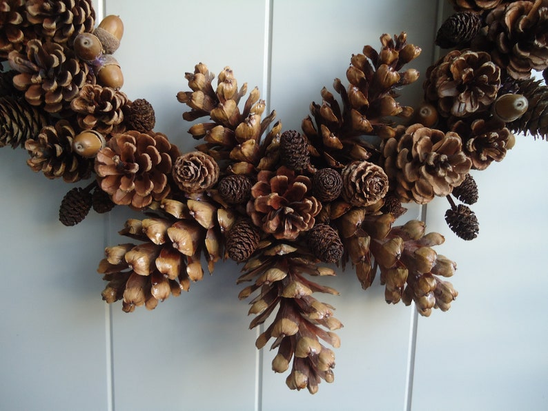 Puede incluir: Una corona de pi&ntilde;as marrones con bellotas y otros elementos naturales. La corona est&aacute; hecha de pi&ntilde;as, bellotas y otros elementos naturales. La corona es de color marr&oacute;n natural.