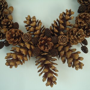 Puede incluir: Una corona de pi&ntilde;as marrones con una variedad de pi&ntilde;as y bellotas. La corona est&aacute; hecha de materiales naturales y es perfecta para un estilo de decoraci&oacute;n r&uacute;stico o de granja.