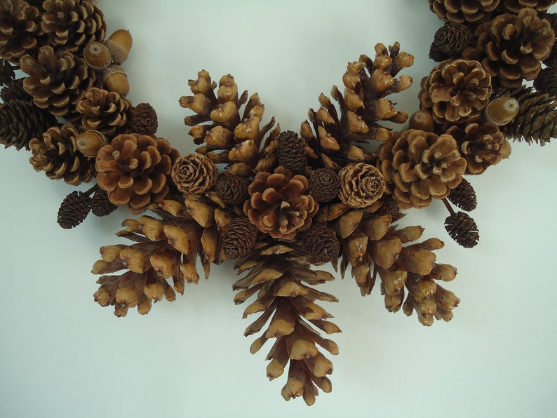 Puede incluir: Una corona de pi&ntilde;as marrones con una variedad de pi&ntilde;as y bellotas. La corona est&aacute; hecha de materiales naturales y es perfecta para un estilo de decoraci&oacute;n r&uacute;stico o de granja.
