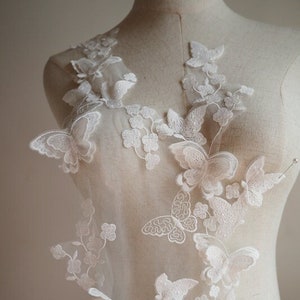 Puede incluir: Tela de encaje blanca con un delicado diseño de mariposa. La tela es transparente y tiene una textura suave y fluida. Las mariposas están bordadas en un patrón detallado y están dispersas por toda la tela.