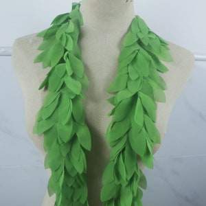 Könnte beinhalten: Zwei Stränge aus hellgrünen Stoffblättern fallen kaskadenartig über eine Schaufensterpuppe. Die Blätter sind geschichtet und bilden eine strukturierte, blattreiche Girlande. Die Blätter haben eine leuchtende, einfarbige grüne Farbe.