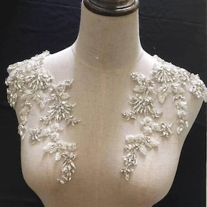 May include: A pair of silver beaded appliques with a floral design. The appliques are made of small, sparkling beads and are perfect for adding a touch of glamour to any garment.