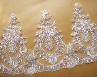 May include: Close-up of white lace trim with a repeating floral and leaf design. The lace features a detailed pattern with a scalloped edge, perfect for bridal wear or other decorative projects.