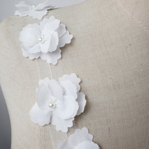 May include: White floral lace trim with pearl embellishments. The trim features delicate, layered flowers with a soft, feminine aesthetic.