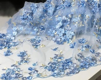 Può includere: Tessuto di tulle azzurro chiaro con ricamo floreale 3D. I fiori sono di una tonalità di blu leggermente più scura e hanno una texture simile al velluto.
