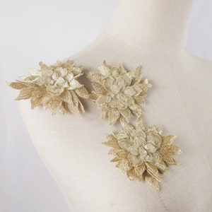 Puede incluir: Tres apliques florales dorados con un diseño delicado e intrincado. Los apliques están hechos de una tela suave y ligera y tienen un brillo sutil.