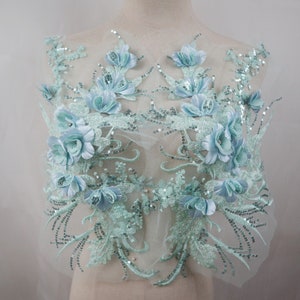 May include: A light blue floral applique with sequins and 3D flowers. The applique is on a sheer mesh fabric.
