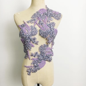May include: A purple and silver beaded applique with a floral design. The applique is on a white mannequin form.