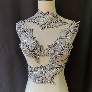 May include: A set of three rhinestone embellishments for clothing or accessories. The embellishments are made of clear rhinestones on a black mesh backing. The embellishments are shaped like a collar, a pair of wings, and a waist band.