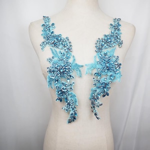May include: Two turquoise floral appliques with intricate bead and crystal embellishments. The appliques are arranged in a symmetrical design, featuring clusters of sparkling beads and crystals. The design is ideal for embellishing garments or accessories.
