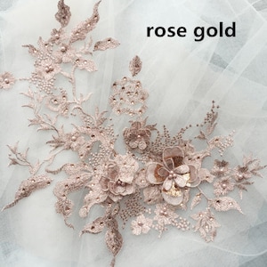 Op de afbeelding: Roze gouden kant applique met delicate bloemenmotieven en parel accenten. De applique heeft een grote bloem met een paillettencentrum en kleinere bloemen eromheen.