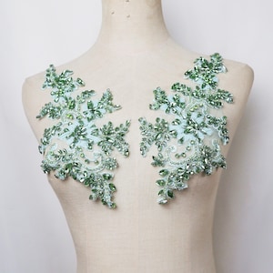 Puede incluir: Dos aplicaciones de encaje con cuentas verdes y azul claro con un diseño floral. Las aplicaciones están en un maniquí blanco.