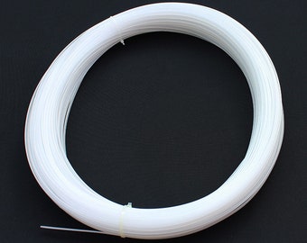 May include: A coiled bundle of white plastic filament, tightly wound into a circular shape. The filament appears to be thin and flexible, with a smooth texture. The bundle is secured with a white plastic tie. The background is a solid black.