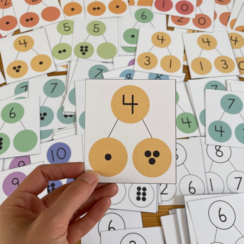 May include: A white card with a yellow circle containing the number "4" at the top. Below the circle are two smaller yellow circles, one with a single black dot and the other with three black dots. This card is part of a set of cards that teach children about numbers and counting.