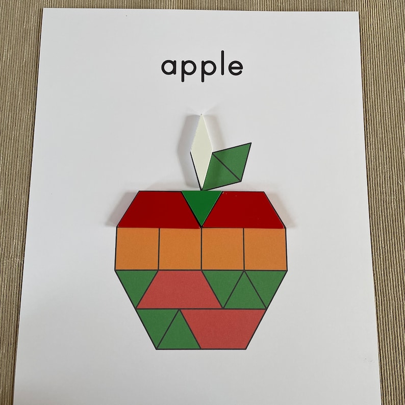 May include: A colorful paper apple made from geometric shapes. The apple is red, orange, green, and pink. The word "apple" is printed above the apple.