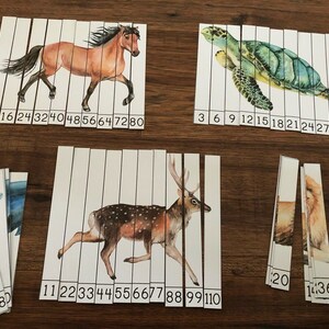 May include: A set of 10 puzzle pieces featuring different animals, including a horse, deer, turtle, dolphin, and lion. Each piece has a number printed on it, ranging from 3 to 110. The pieces are arranged in rows on a wooden surface.