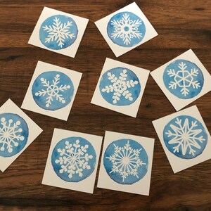 May include: Nine blue watercolor cards with white snowflake designs. Each card features a different snowflake design.