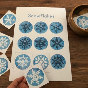 May include: A set of nine blue and white snowflake cards with the word "Snowflakes" printed at the top. The cards are arranged in a grid pattern on a white background.