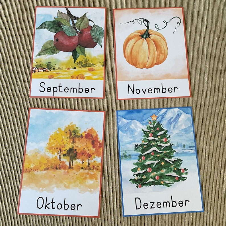 May include: Four watercolor illustrations on cards depicting the months of September, October, November, and December. September shows red apples on a branch, October shows a group of trees with fall foliage, November shows a pumpkin, and December shows a Christmas tree with snow.