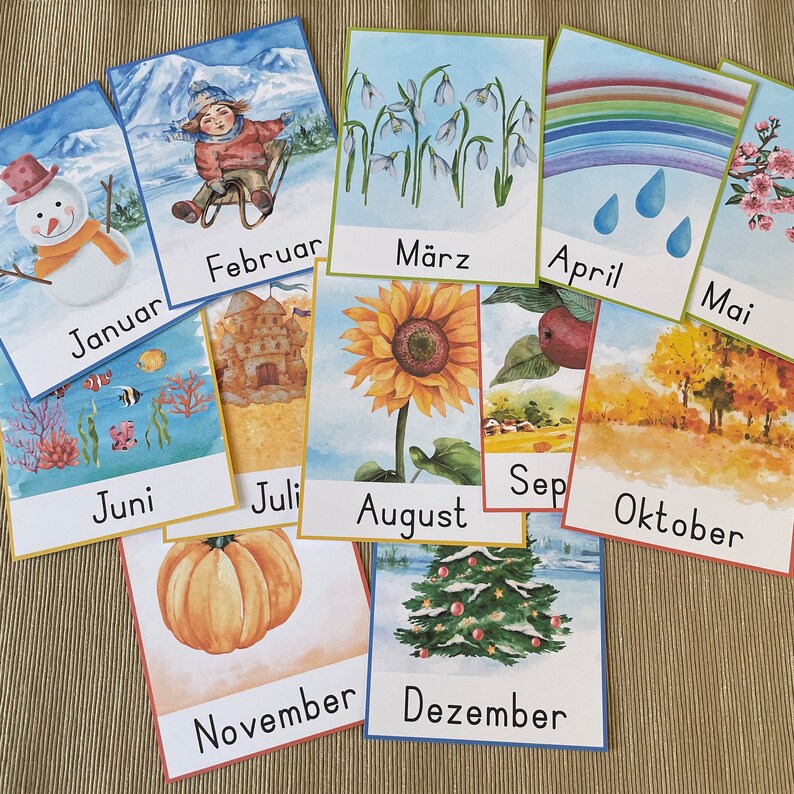 May include: Twelve illustrated cards with the months of the year in German. Each card features a different image representing the month, such as a snowman for January, a sunflower for August, and a Christmas tree for December.